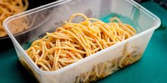 a plastic container filled with pasta sitting on top of a green tablecloth covered floor