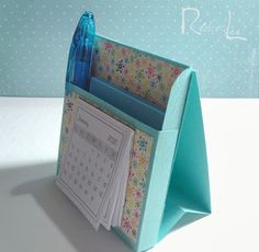 a desk with a blue pen holder and calendars on the front, next to a wallpapered background