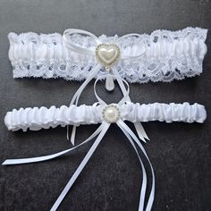 Our classic White Garter Set is made of fine satin fabric. It has the classic ruffled design with soft elastic lace trim. A bejeweled heart button with dangling pearl and ribbons accentuate the middle.  This is an elegant addition to your wedding accessories that will definately make as a timeless keepsake.  It includes a thinner twin pair for tossing at the reception. Features: Set of two garters Material: Polyester, lace, rhinestone buttons Measurements: Approximately 7 inches in diameter and Wedding Leg Garter, White And Black Lace Garter, Garter Set Wedding, White Garter, White Garter Belt Vintage, White Lace Garter, White Garters, Bridal Garter Lace, Wedding Garter Set