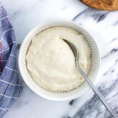 a white bowl filled with sauce next to a wooden spoon on top of a marble counter