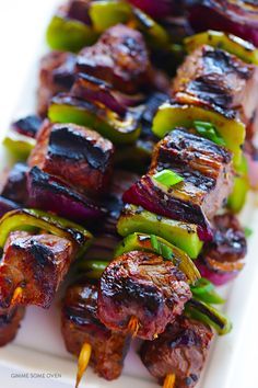 several skewers of meat and vegetables on a white plate