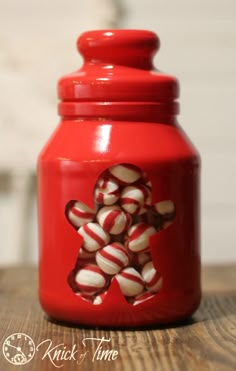 a red jar filled with candy canes on top of a wooden table