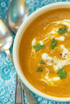 a bowl of soup with sour cream and garnishes on top, next to silver spoons