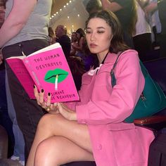 a woman sitting down reading a book with her legs crossed and holding a green umbrella