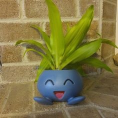 a potted plant with a smiley face on the ground next to a brick wall