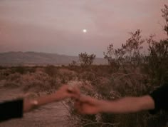 two hands reaching out towards each other in the desert at dusk with mountains in the background