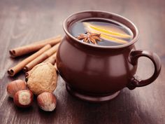 a brown cup filled with liquid surrounded by cinnamons and nuts