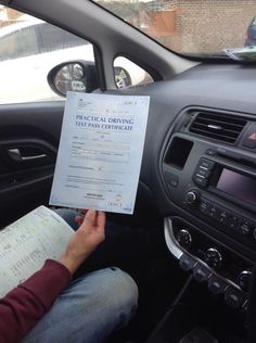 a person sitting in the driver's seat of a car reading a driving manual