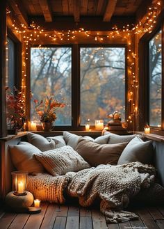 a cozy window seat with candles on the windowsill and blankets in front of it