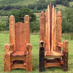 two carved wooden chairs sitting on top of a lush green field with trees in the background