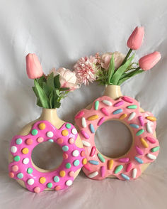 two vases with flowers and doughnuts in them on a white sheeted surface