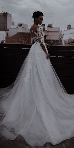 a woman in a wedding dress standing on top of a roof with her back to the camera