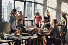 a group of people gathered around a computer screen in an office setting with brick walls and floor to ceiling windows