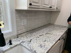 a man standing in front of a kitchen counter with white cabinets and granite counter tops