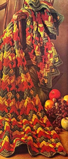 a crocheted blanket sitting on top of a wooden chair next to fruit and vegetables