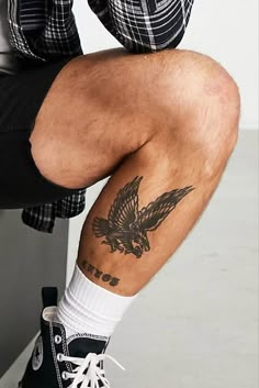 a man sitting on top of a stool with his legs crossed and an eagle tattooed on the leg