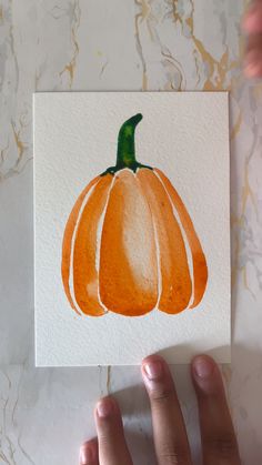 a hand holding up a card with an orange pumpkin on it