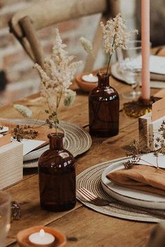 a wooden table topped with plates and vases filled with flowers