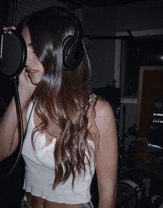 a woman with headphones on in front of a microphone and recording equipment behind her