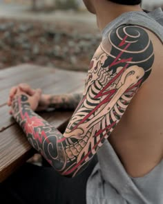 a man sitting on a wooden bench with tattoos on his arm and shoulder, looking at the camera