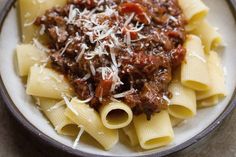 pasta with meat sauce and parmesan cheese in a bowl on a plate next to bread