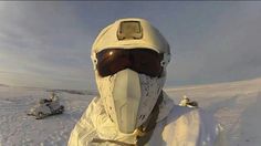 a person wearing a white jacket and goggles in the snow with other people on sleds behind them