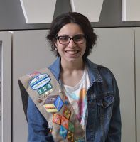 a woman wearing a jean jacket with patches on her chest and smiling at the camera