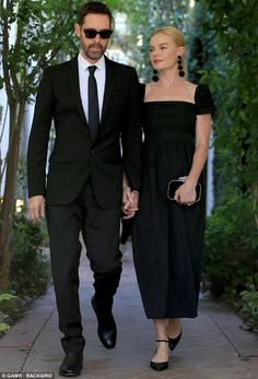 a man and woman are walking down the sidewalk holding hands while dressed in black attire