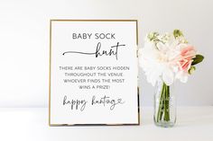 a baby sock hunt sign next to a vase with flowers in it on a table