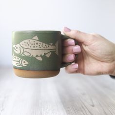 a hand holding a green coffee cup with fish on it