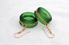 two green rings with gold chains attached to them sitting on a white surface, next to each other