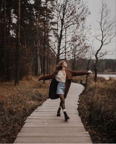 a woman walking down a wooden walkway in the woods with her arms spread wide open