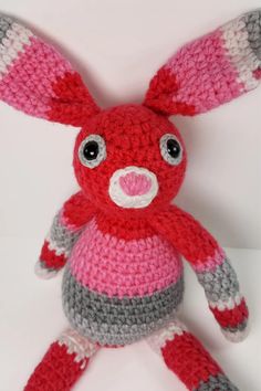 a crocheted red and gray stuffed animal with big eyes sitting on a white surface