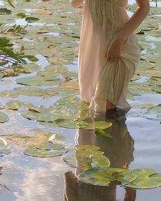 a woman in a dress is standing in the water with lily pads on her feet