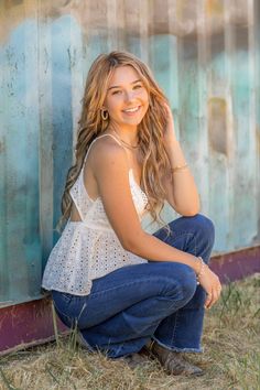 a beautiful young woman sitting on the ground in front of a metal wall smiling at the camera