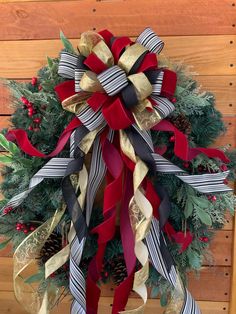 a christmas wreath hanging on the side of a wooden wall with red, white and black ribbons