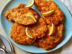 some fried food on a blue plate with lemon wedges and silverware next to it