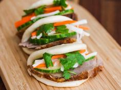 three sandwiches with veggies on them sitting on a cutting board