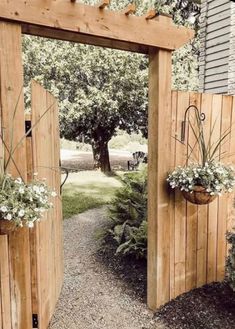 an open wooden gate with potted plants on each side and two hanging planters