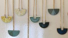 several necklaces hanging on a wall with different shapes and colors in gold, green, blue, and silver