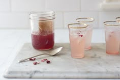 three glasses filled with liquid sitting on top of a marble tray next to a spoon