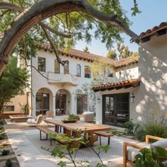 an outdoor patio with tables and chairs next to a tree in front of a house