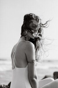 a woman in a bathing suit sitting on the beach with her hair blowing in the wind