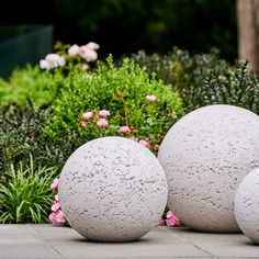 three cement balls sitting on the ground in front of some bushes and flowers with pink flowers behind them