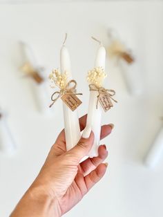 someone holding two candles in their hand with tags attached to the top and bottom of them