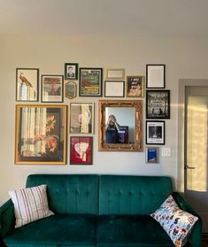 a green couch sitting in front of a wall filled with pictures and framed photos on it