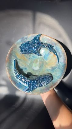 a hand holding a blue and white bowl with two bananas on the bottom, in front of a gray background