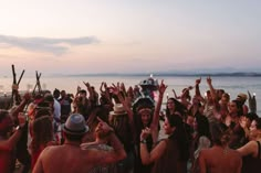 a group of people standing on top of a beach next to the ocean with their arms in the air