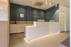 the front desk of an office with blue walls and white counter tops is illuminated by recessed lighting