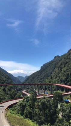 a road going over a bridge in the middle of a mountain range with trees on both sides